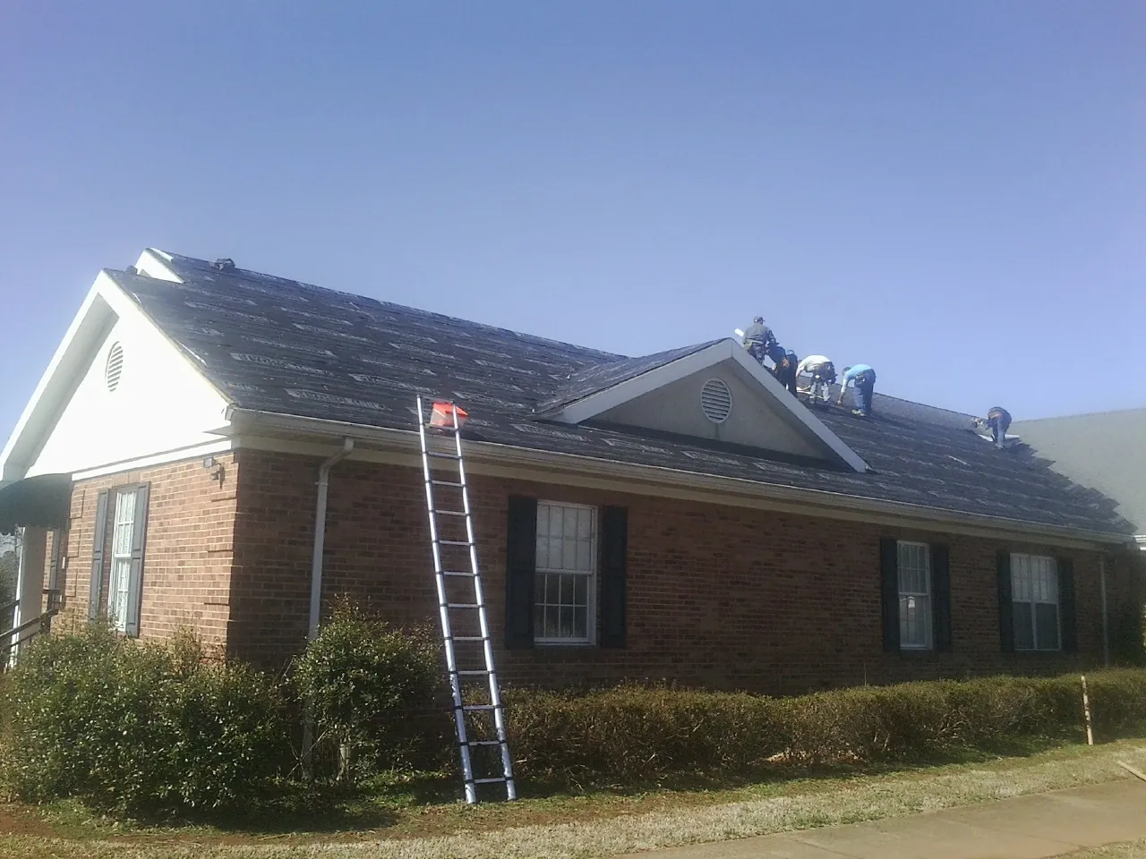 Crew tearing shingles off a brick ranch roof with a ladder set — Metal Roof Repair work by our crew in Marstons Mills