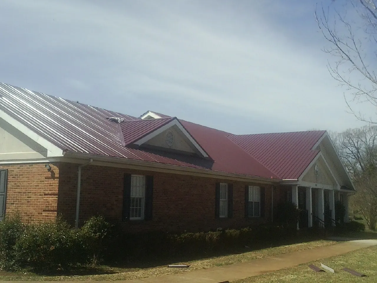 Red metal roof with gabled entries on a long brick building, from a Hail Damage Roof Repair job in Marstons Mills