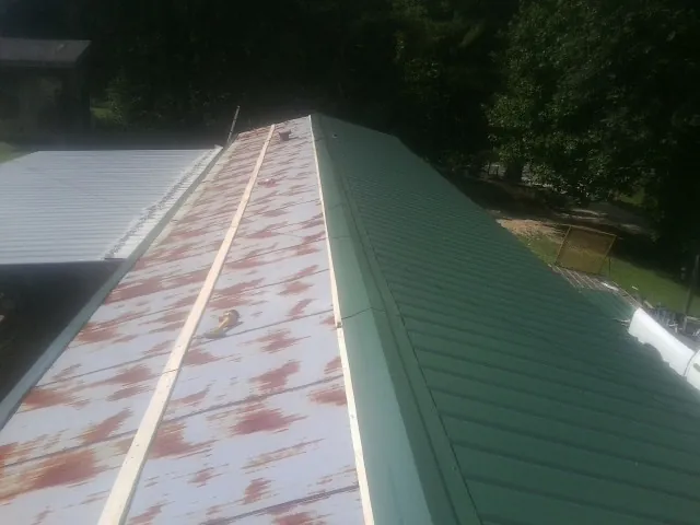 Old rusted panels beside newly installed green metal roofing — Wind Damage Roof Repair by Roofing Brothers in Marstons Mills