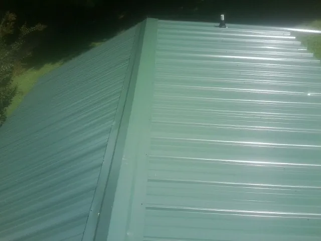 New green metal panels meeting at the ridge of a roof — Flat Roof Repair work by our crew in Marstons Mills