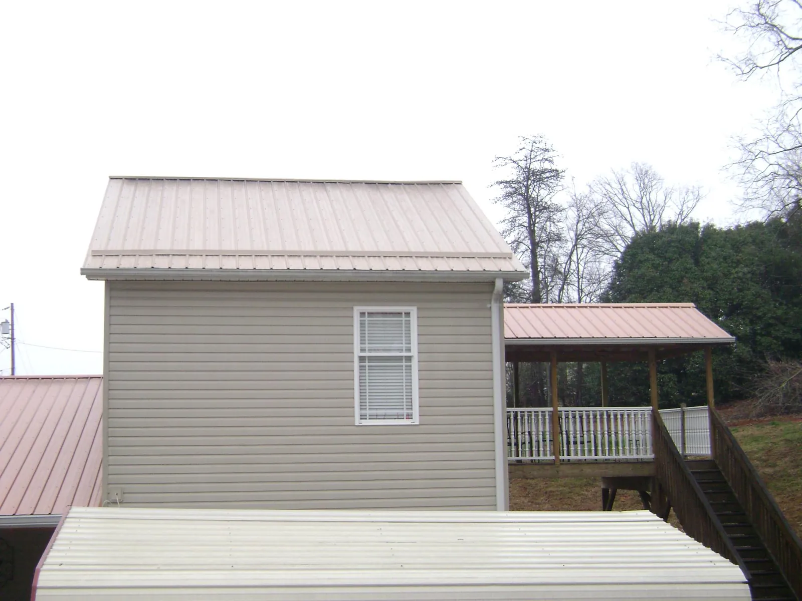 Tan metal roofs on a two story addition and attached porch, from a Roof Replacement job in Marstons Mills